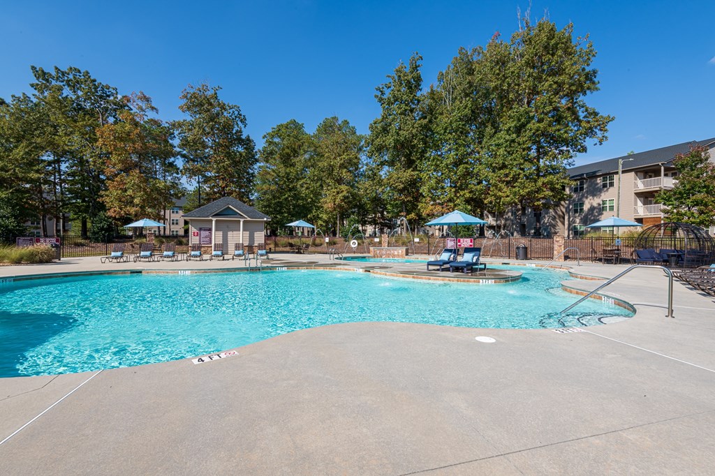 A large swimming pool surrounded by trees and a building in the background.