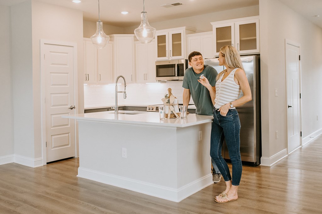 Home Interior A man and woman are standing in a kitchen with a sink and a refrigerator.