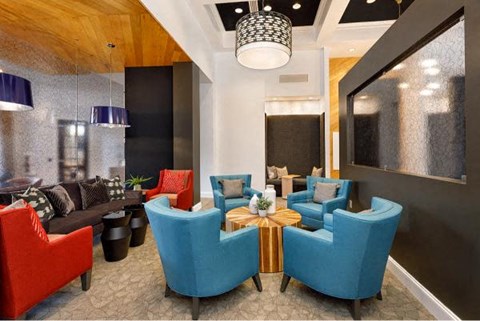 A modern living room with a mix of red and blue chairs and a wooden ceiling.