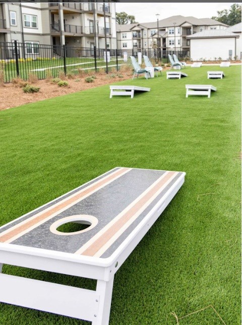 A cornhole game set up on a grassy area in front of apartment buildings.