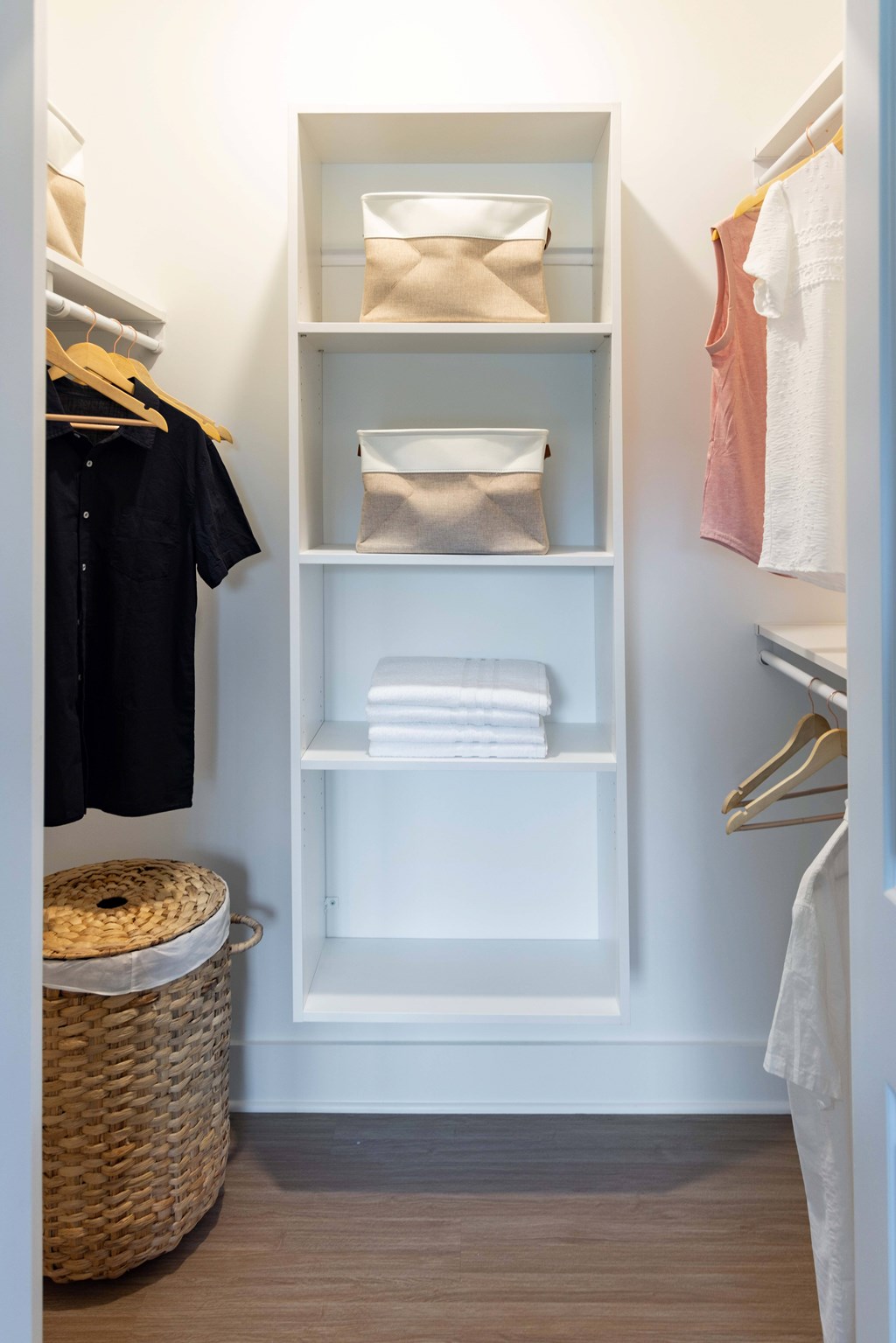 A white closet with a basket and a black shirt hanging on a hanger.