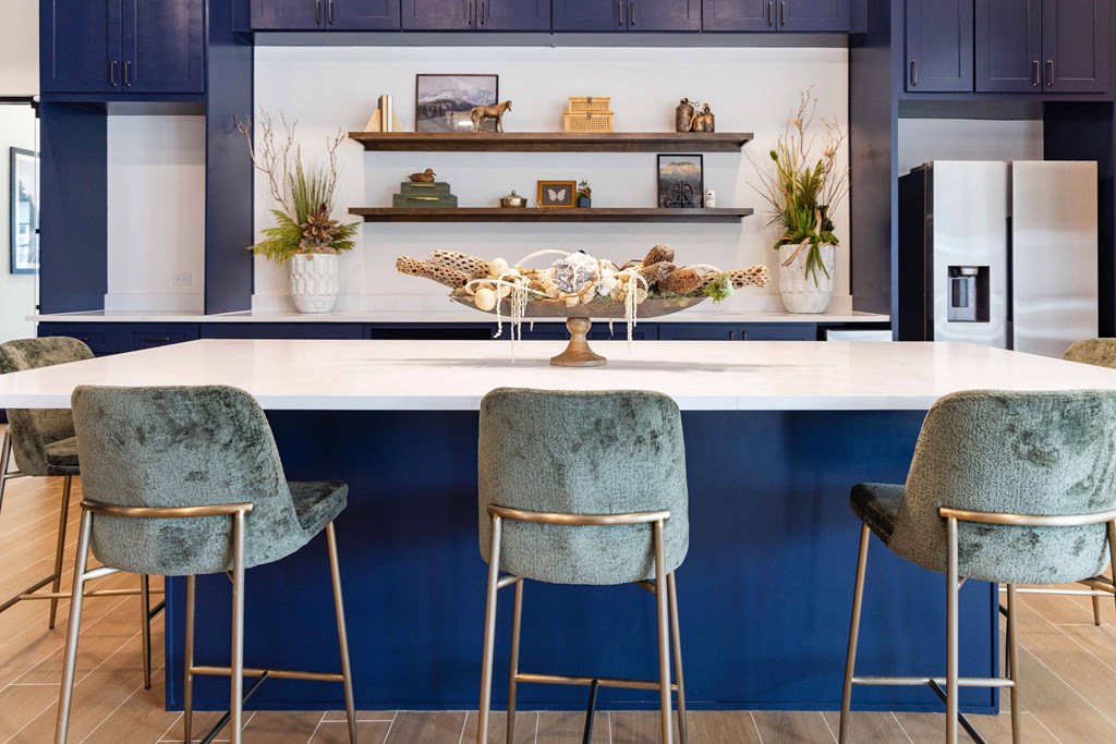 Large kitchen with blue cabinets and a white island with three chairs.