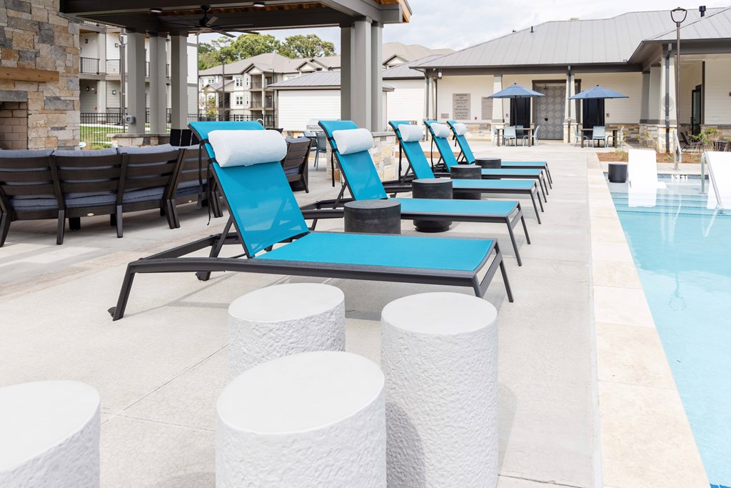 A poolside area with blue lounge chairs and white stools.