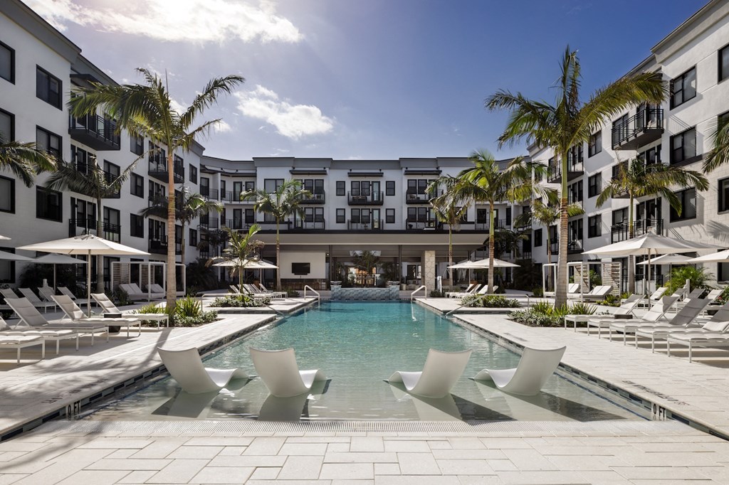 A large pool surrounded by lounge chairs and palm trees.