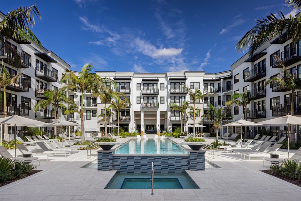 A large swimming pool in the middle of a resort surrounded by lounge chairs.