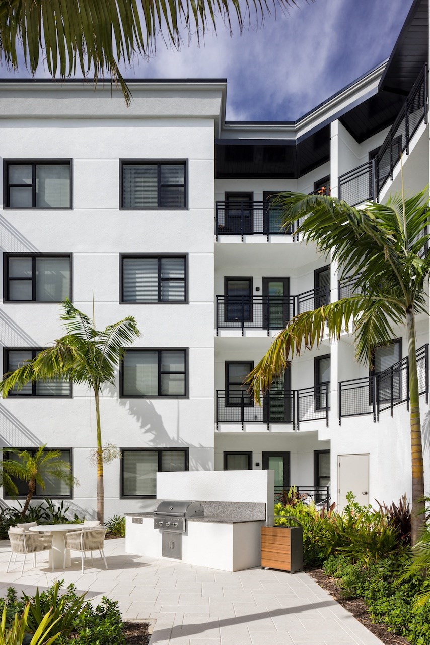 A white building with black railings and windows surrounded by green plants.