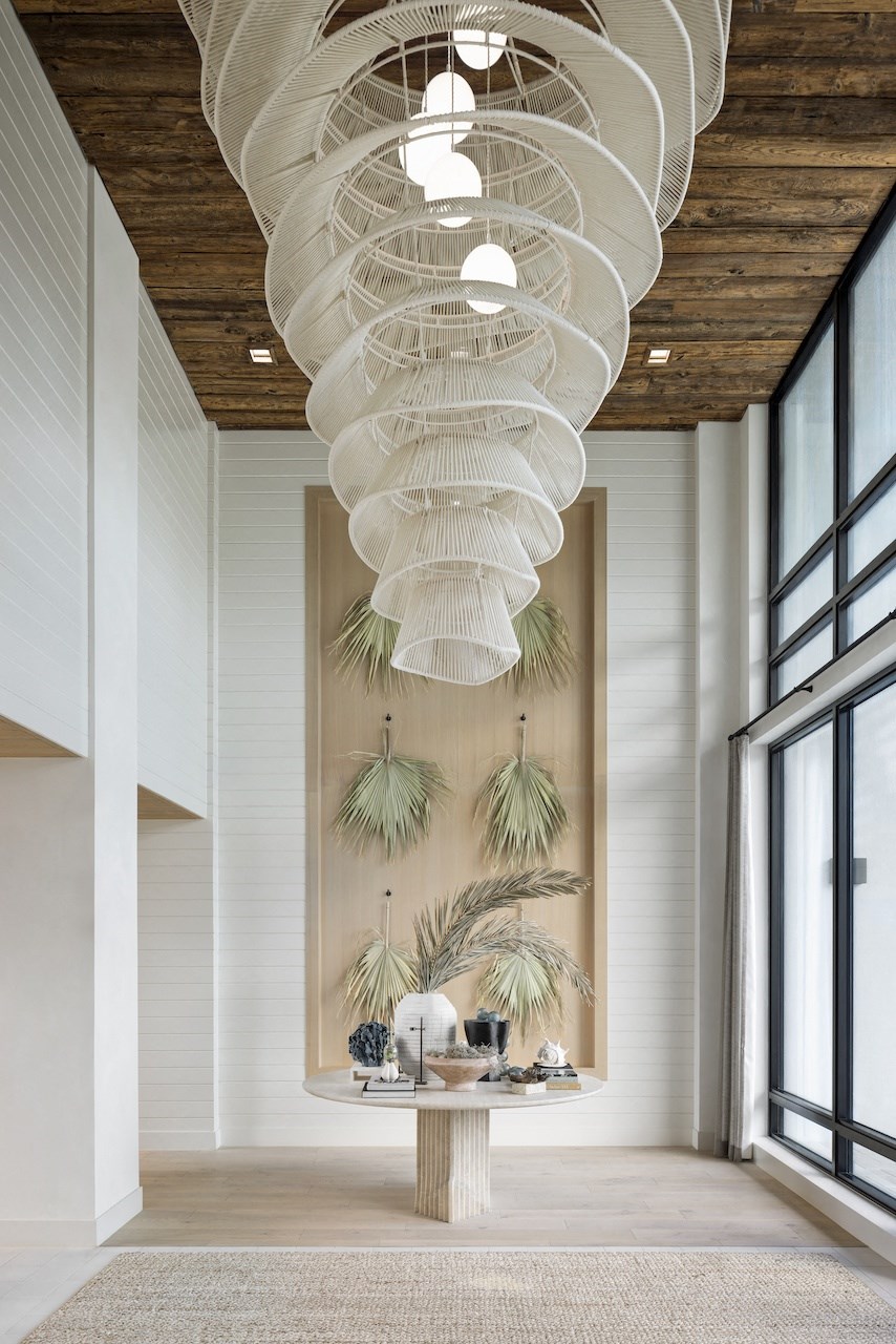 A white hanging light fixture hangs from a wooden ceiling above a table with a plant on it.