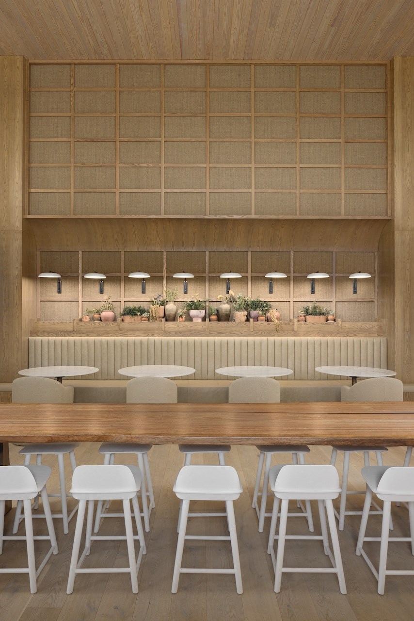 A long wooden table with white chairs in front of a wall with a row of lights.