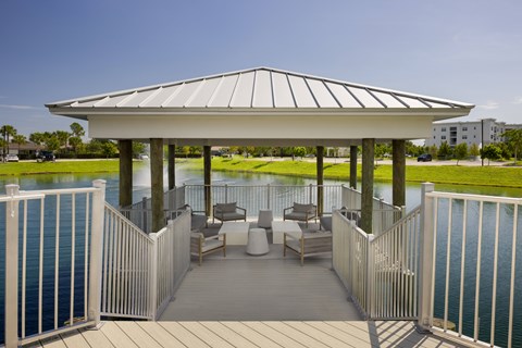 A gazebo with a white roof is surrounded by a white fence and has a deck with chairs and a table.