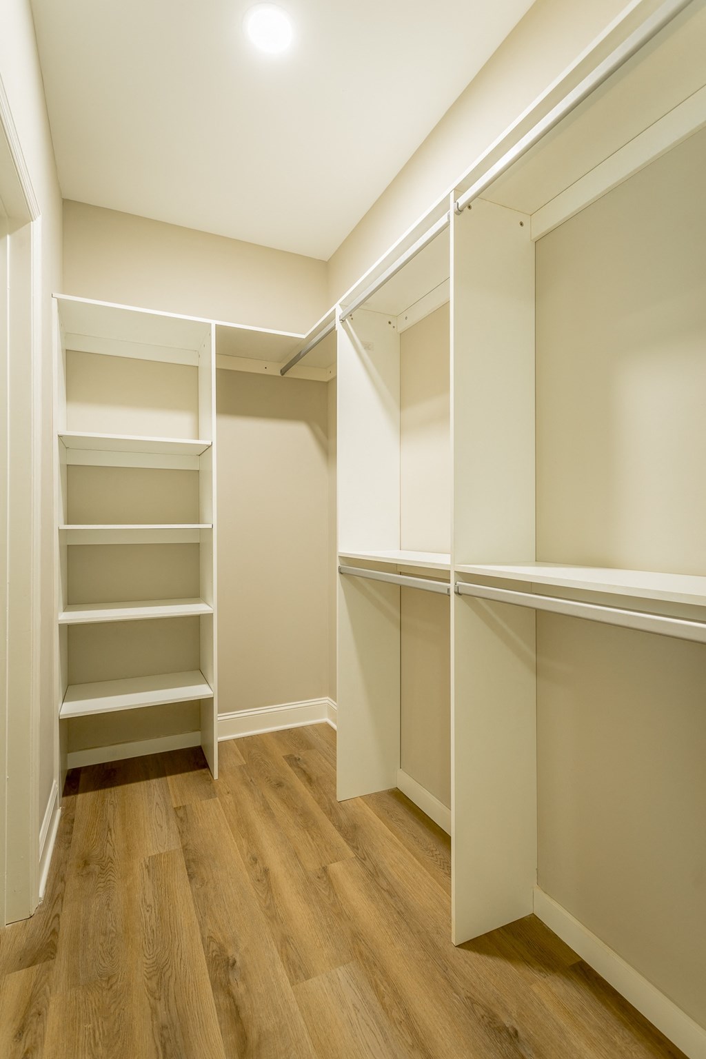 a walk in closet with white shelving and a wood floor