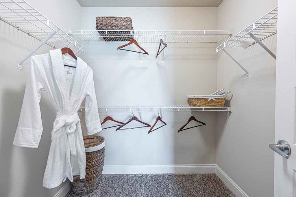 a walk in closet with a white robe and hangers and a basket