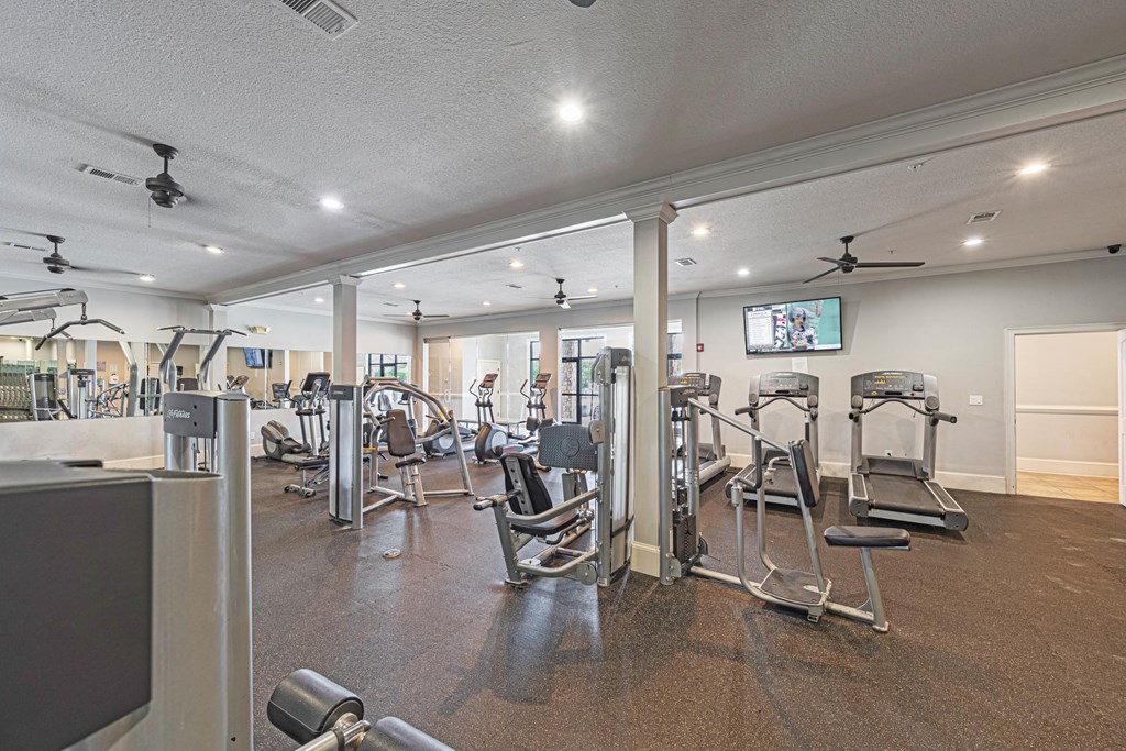 a gym with cardio machines and weights on the floor and a tv