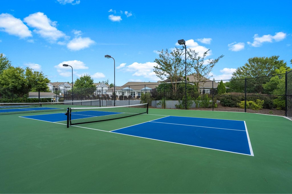 two tennis courts with houses in the background on a sunny day