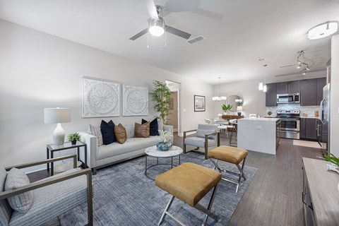 a living room with couches and chairs and a kitchen with a ceiling fan
