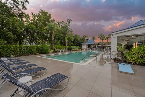 a swimming pool with blue lounge chairs and a poolside spa with a purple sky