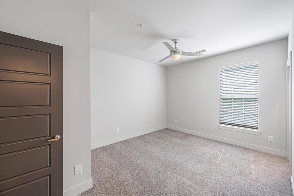 an empty bedroom with a ceiling fan and a window