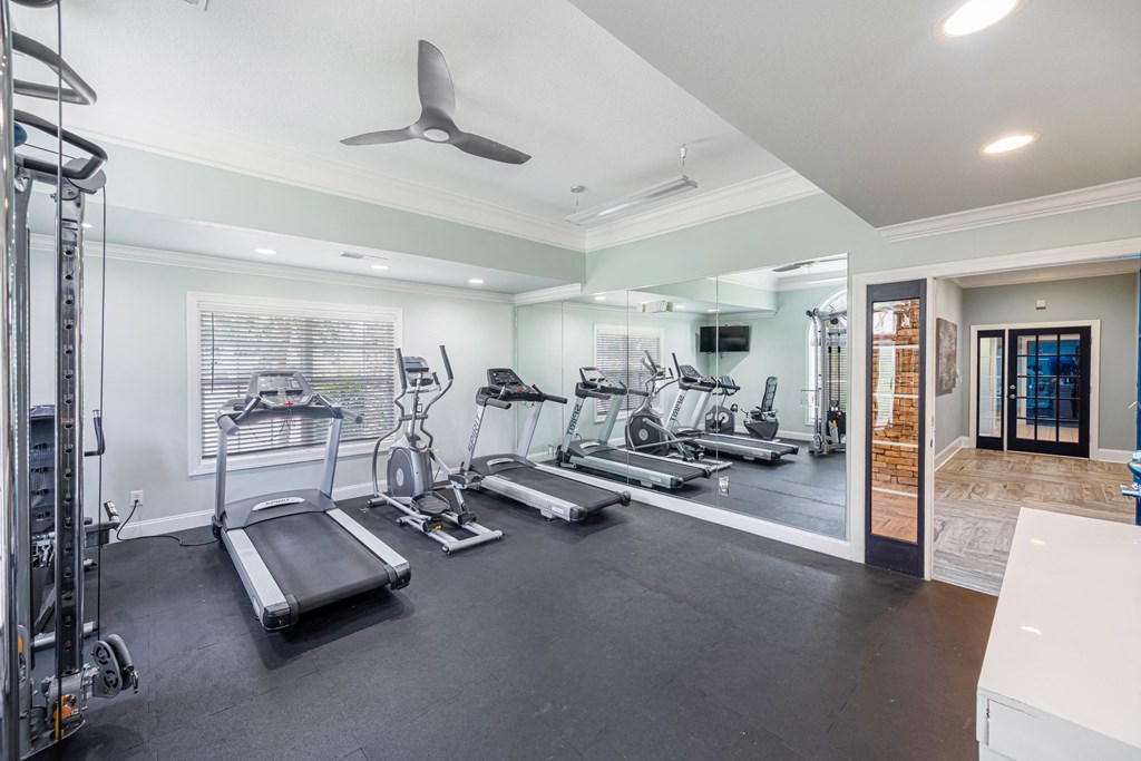 a gym with cardio machines and a ceiling fan