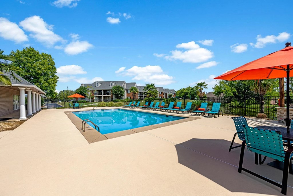 our resort style swimming pool is surrounded by lounge chairs and an umbrella