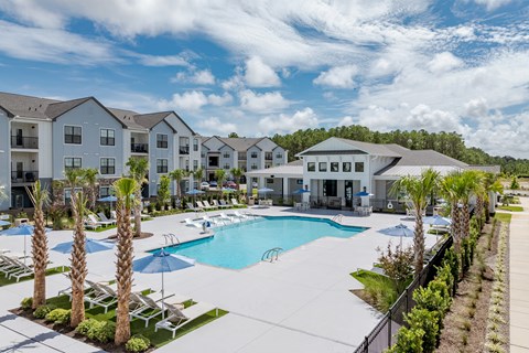 A swimming pool surrounded by palm trees and lounge chairs in a residential area at Evolve Holly Ridge Apartments in Holly Ridge, NC.
