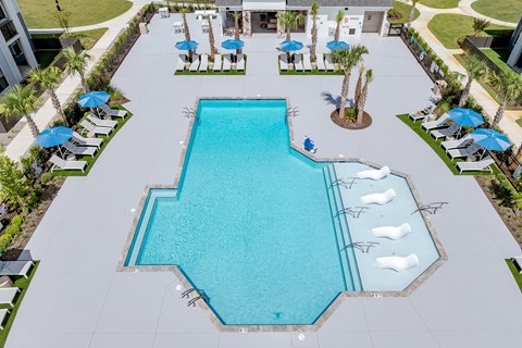 A large outdoor swimming pool surrounded by sun loungers and umbrellas at Evolve Holly Ridge Apartments in Holly Ridge, NC.