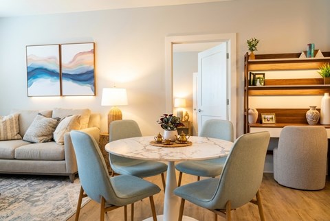 A modern dining room with a round marble table and grey chairs.