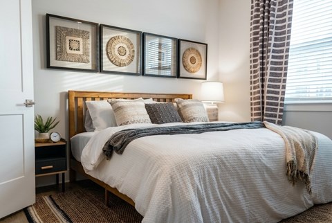 A bedroom with a bed, pillows, a blanket, a nightstand, and a window with curtains.