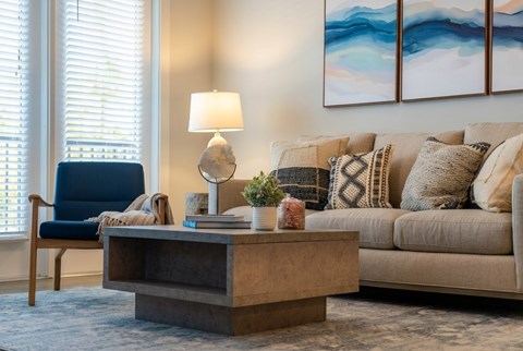A living room with a blue chair, a beige couch, and a painting on the wall.