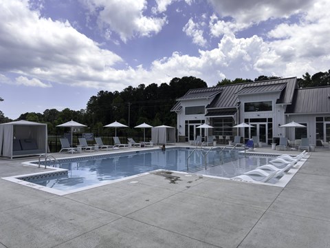 2-Bedroom Luxury Apartments in Myrtle Beach, SC - Anchor Pointe - Resort-Style Swimming Pool With In-Water Loungers, Sun Deck Chairs, Umbrella Seating, White Cabanas, and Clubhouse Building.