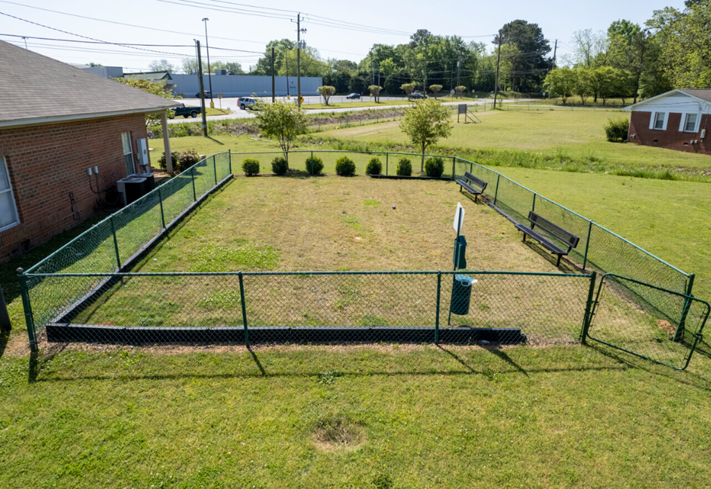 a fenced in batting cage in a grassy field with a house
