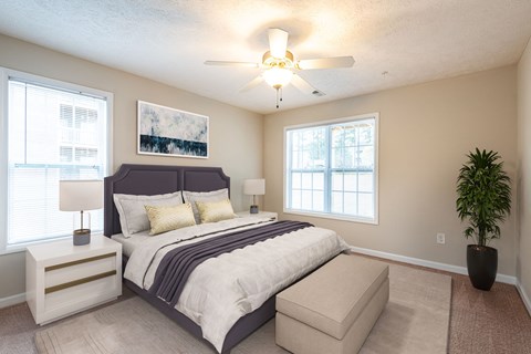 A bedroom with a large bed, a ceiling fan, and a potted plant.