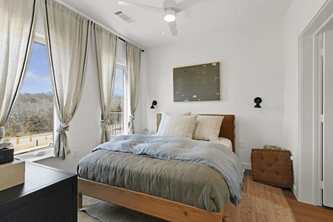 A bedroom with a large bed and a view of the outdoors through the window at Terraces at High Mountain apartments in Huntsville, AL.
