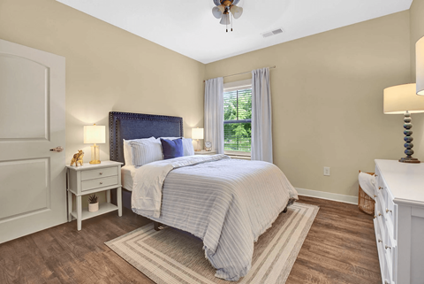 A bedroom with a bed, nightstand, and a window with curtains.