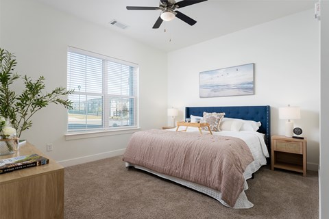 A bedroom with a bed, nightstand, and a plant.