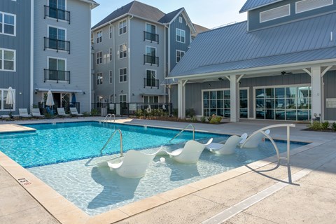 A pool with white chairs and a building in the background.