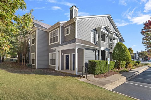 A house with a grey siding and a white trim is surrounded by trees and a sidewalk.