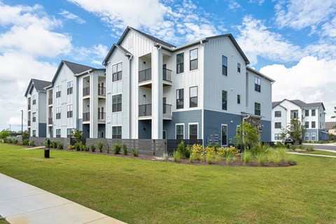 A row of modern apartment buildings with green lawns in front at Evolve Holly Ridge Apartments in Holly Ridge, NC.