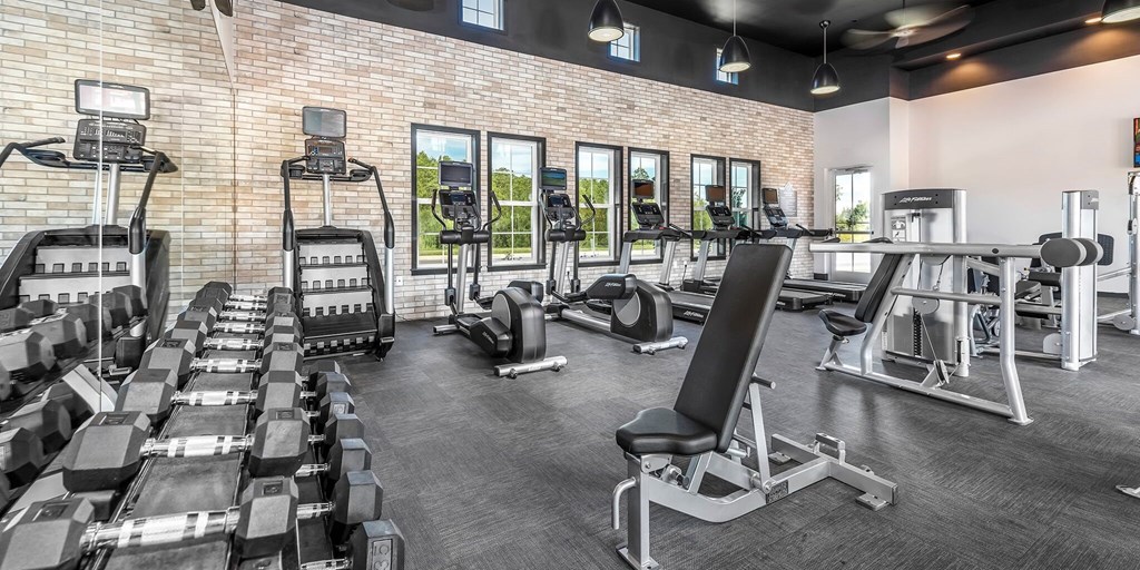 a gym with cardio equipment and weights on a brick wall