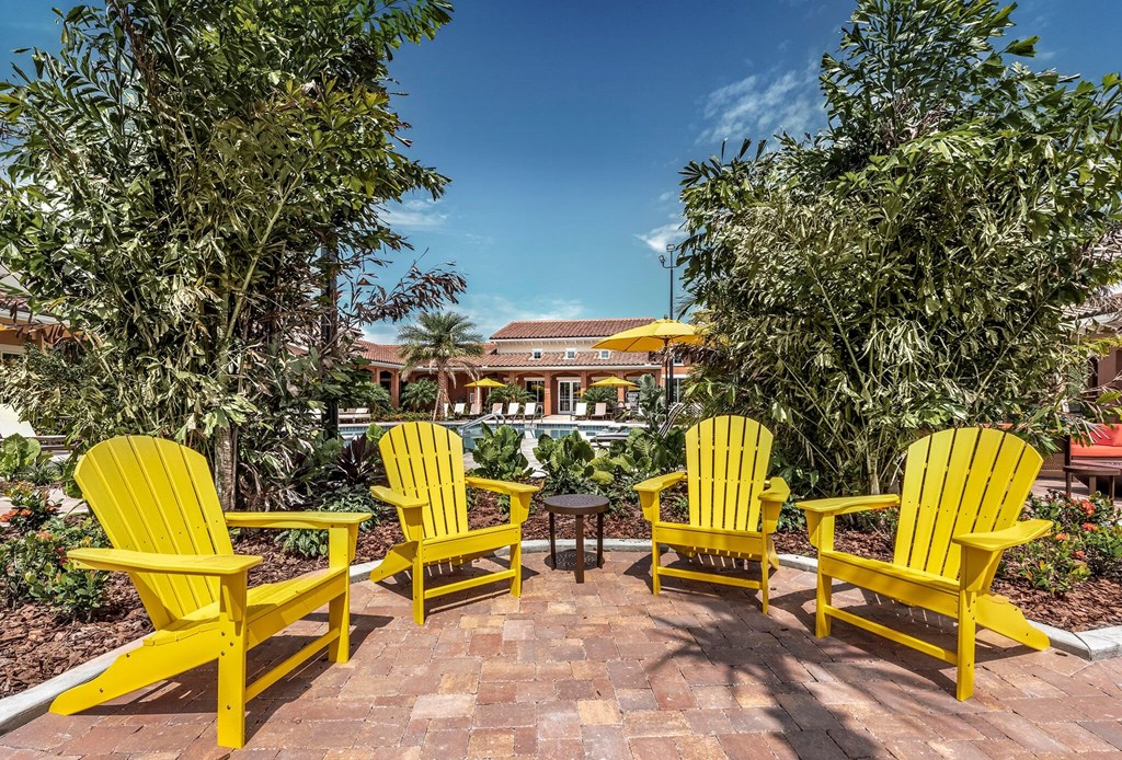 a group of yellow chairs on a brick patio near a swimming pool