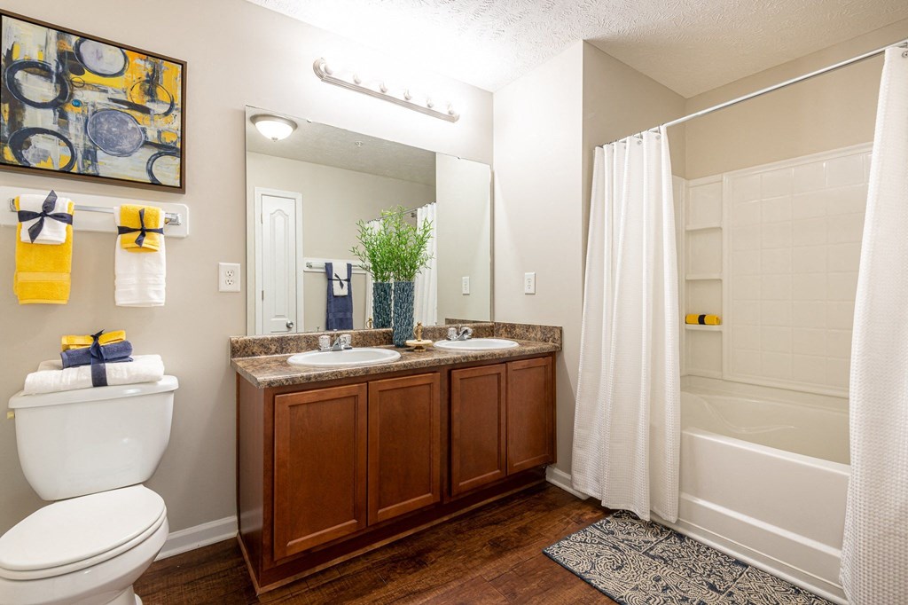 A bathroom with a white toilet, a sink with a brown cabinet, and a shower with a white curtain.