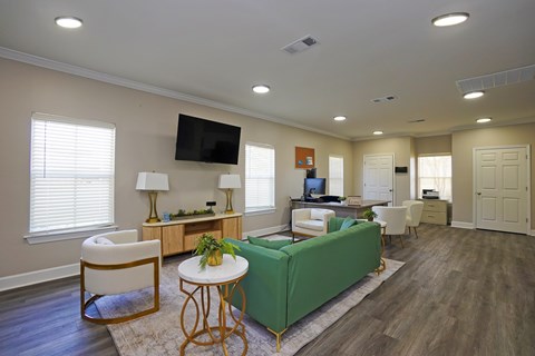 A living room with a green couch, a white chair, and a television mounted on the wall.