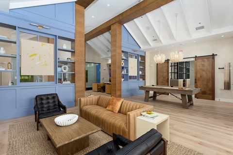 A clubhouse seating area with a black leather chair and a brown sofa at Evolve Holly Ridge Apartments in Holly Ridge, NC.
