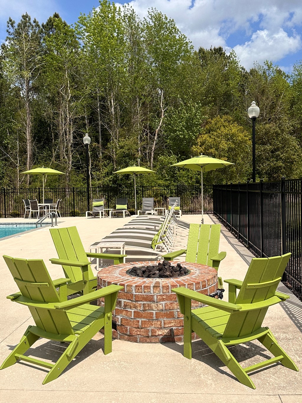 a fire pit with green chairs around it and umbrellas