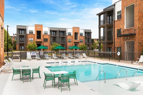 A swimming pool surrounded by chairs and tables in front of apartment buildings.