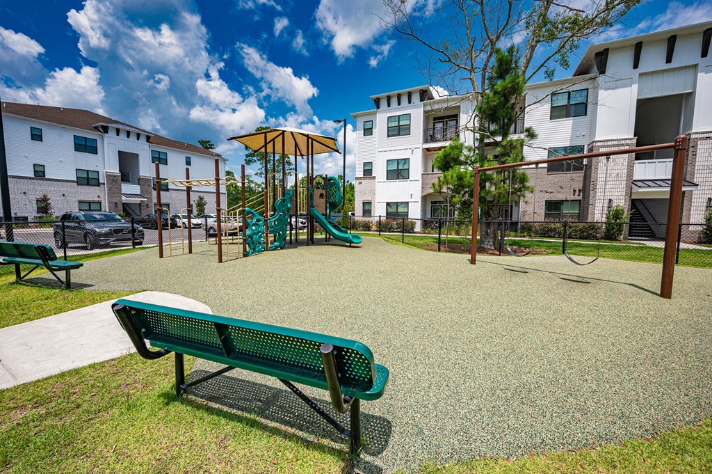 A playground with a green bench and a slide in front of apartment buildings.