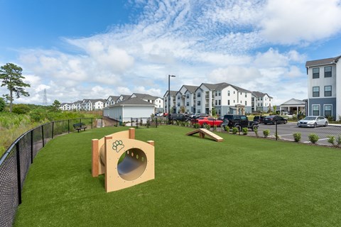 A playground with a slide and a ball pit in the foreground and apartment buildings in the background at Evolve Holly Ridge Apartments in Holly Ridge, NC.