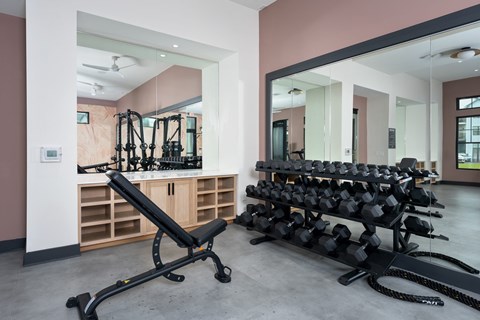 A gym with a mirror, weights, and a bench. at Evolve Holly Ridge Apartments in Holly Ridge, NC