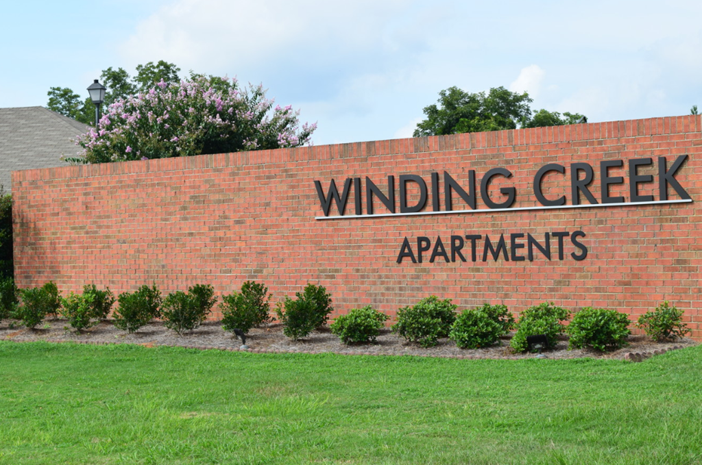 a brick wall with winding creek apartments in front of a lawn