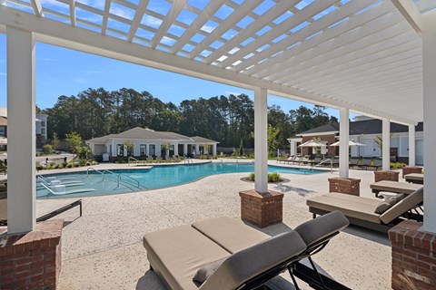 A pool area with a white pergola and lounge chairs.