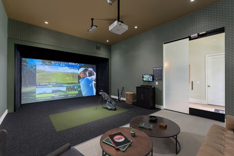 A  game simulator room with a screen and a couch at Evolve Holly Ridge Apartments in Holly Ridge, NC