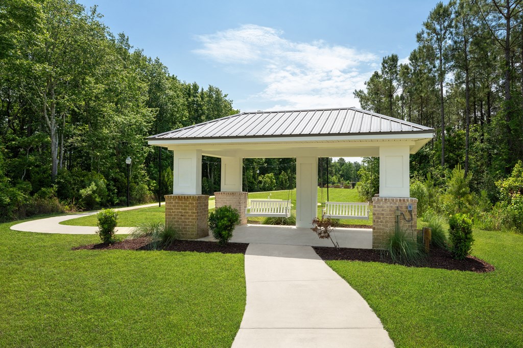 A gazebo is surrounded by a white picket fence and greenery.